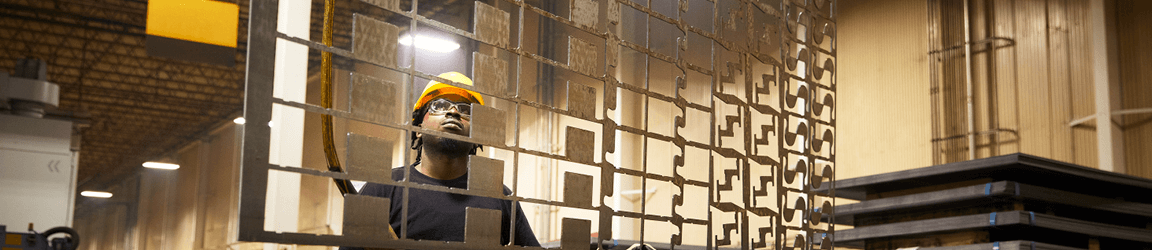 A worker in a black shirt and hard hat looks intently at a metal panel