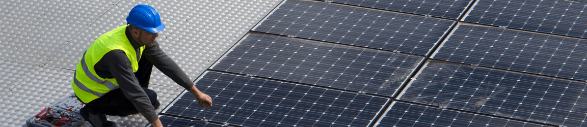 A worker in a hard hat and reflective vest works on a solar panel