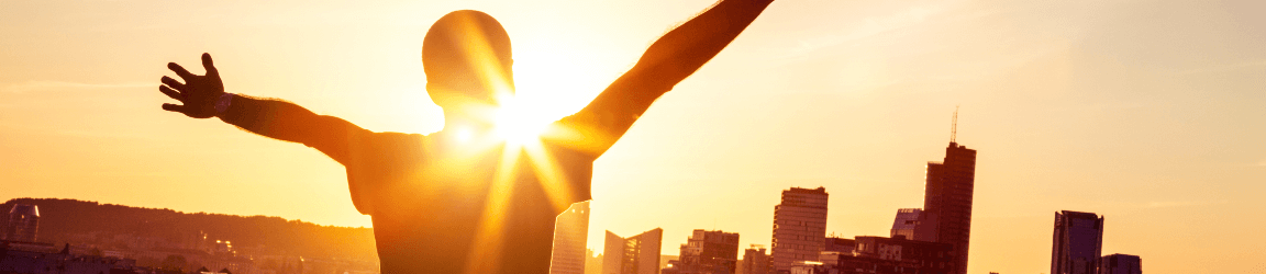 A person looks at a city skyline with their arms stretched as the sun rises.