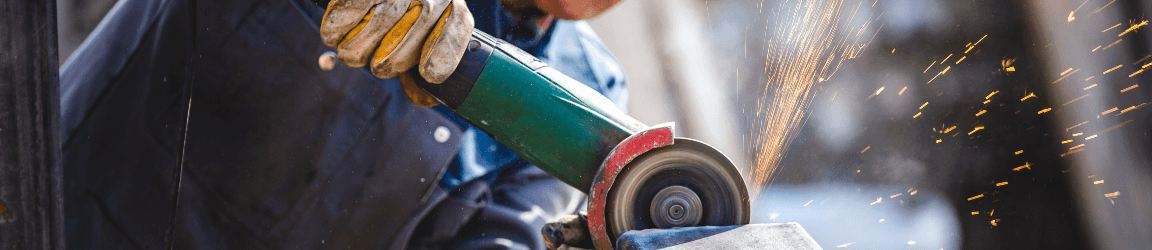 A worker wearing a glove uses a grinder and sparks fly.