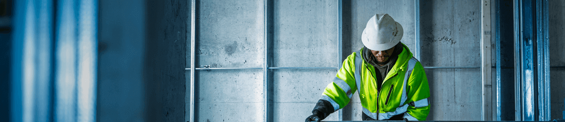 A construction contractor in a hard hat and yellow jacket works on a job site.
