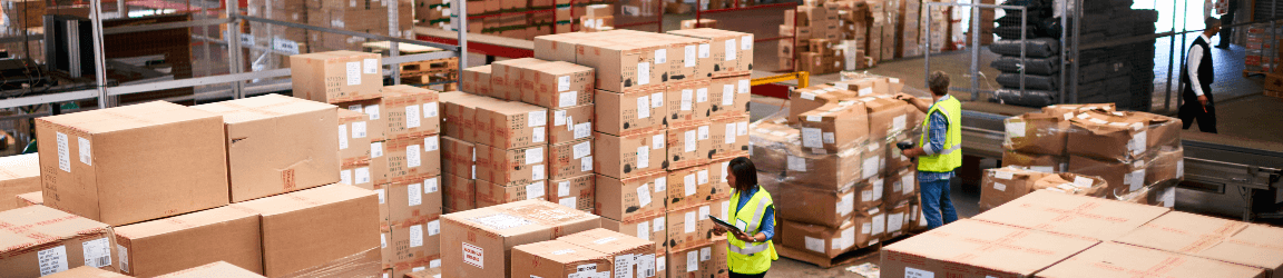 Three workers wearing safety vests organize dozens of boxes for shipment inside of a warehouse.