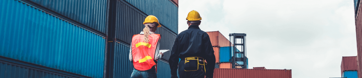 Avec leurs dos tournés, un homme et une femme marche à travers un chantier de conteneur maritime en extérieur.